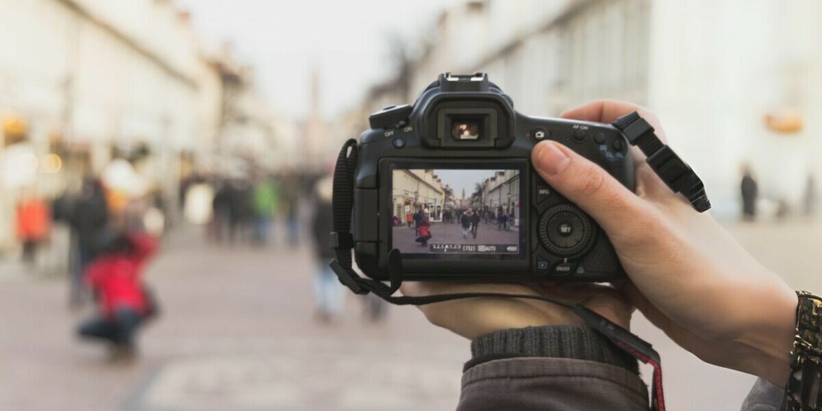 Tendencias da fotografia em 2024: mao de um fotografo com uma camera capturando a imagem de um local movimentado.